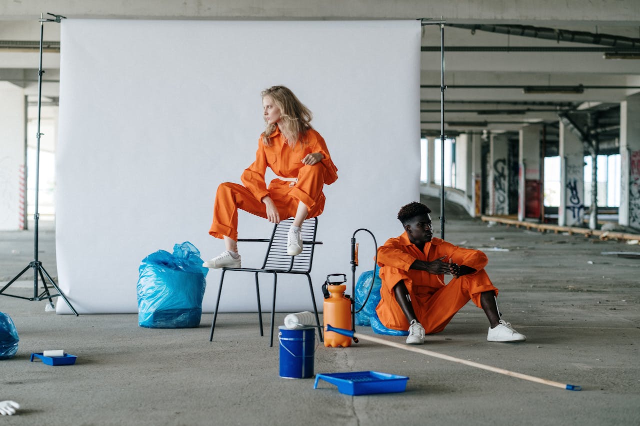 Two workers in orange uniforms pose in an industrial setting, surrounded by cleaning supplies.
